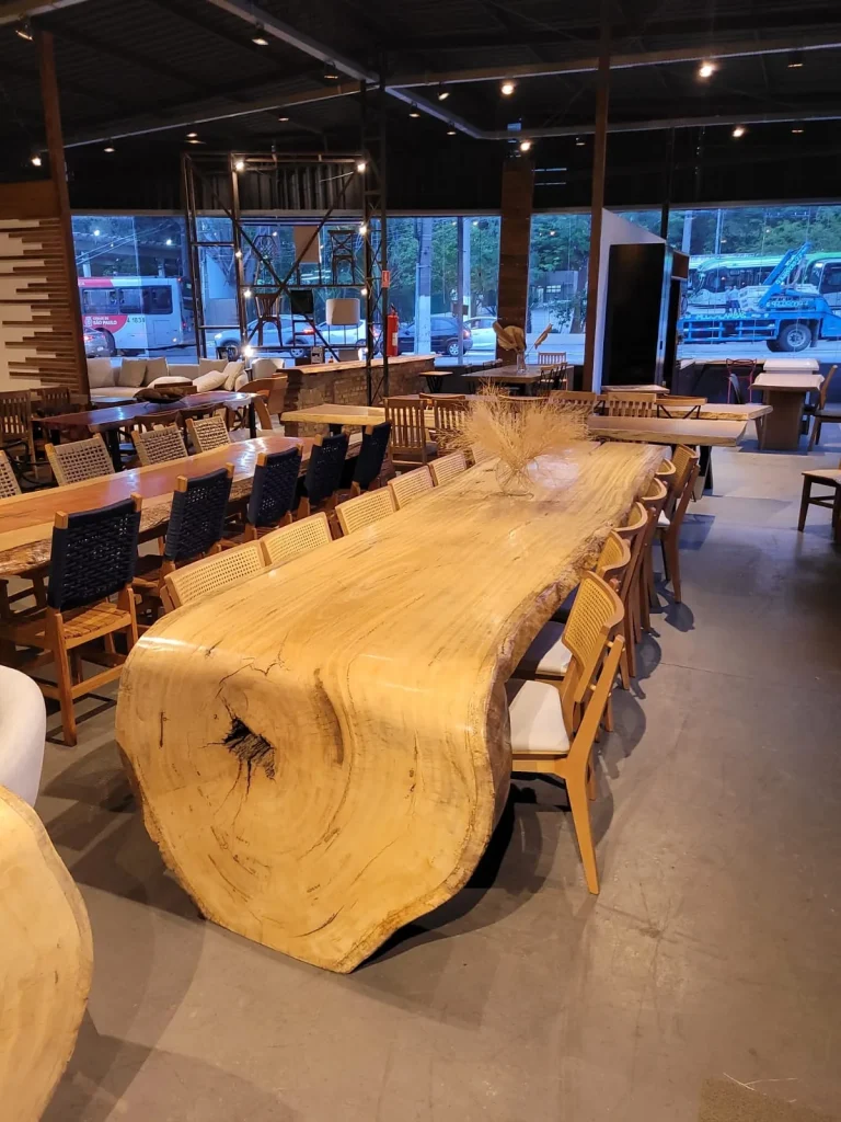 Mesa cascata de madeira maciça amarela em vista lateral, ao lado de outras mesas do showroom, Curitiba