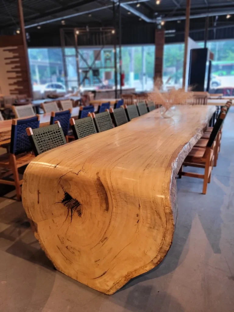 Mesa cascata de madeira maciça clara com lateral em tronco, junto à fachada de vidro da loja em Curitiba